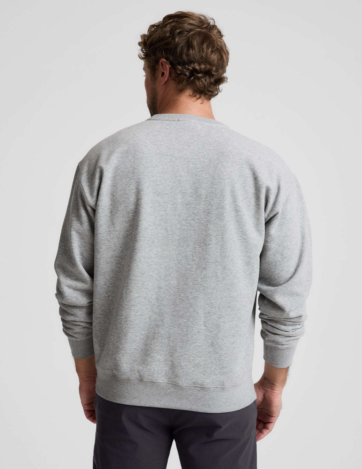Man wearing a gray sweater and black pants against a plain background.