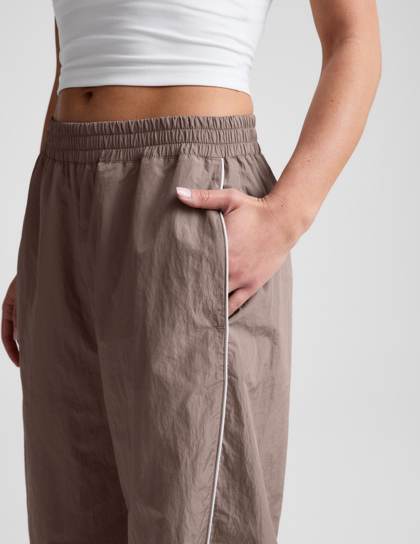 Brown Limitless Mid-Rise Barrel Leg Pant showing gathered elastic waistband, side pocket, and white piping on ripstop fabric.