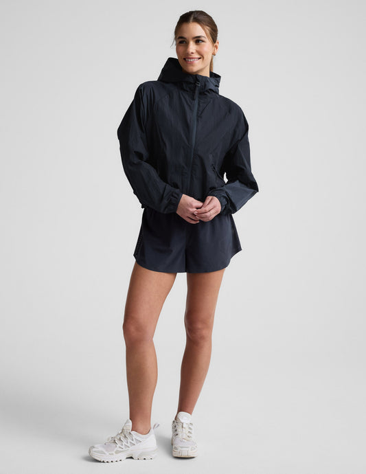Woman wearing a blue hooded jacket and shorts against a plain background.