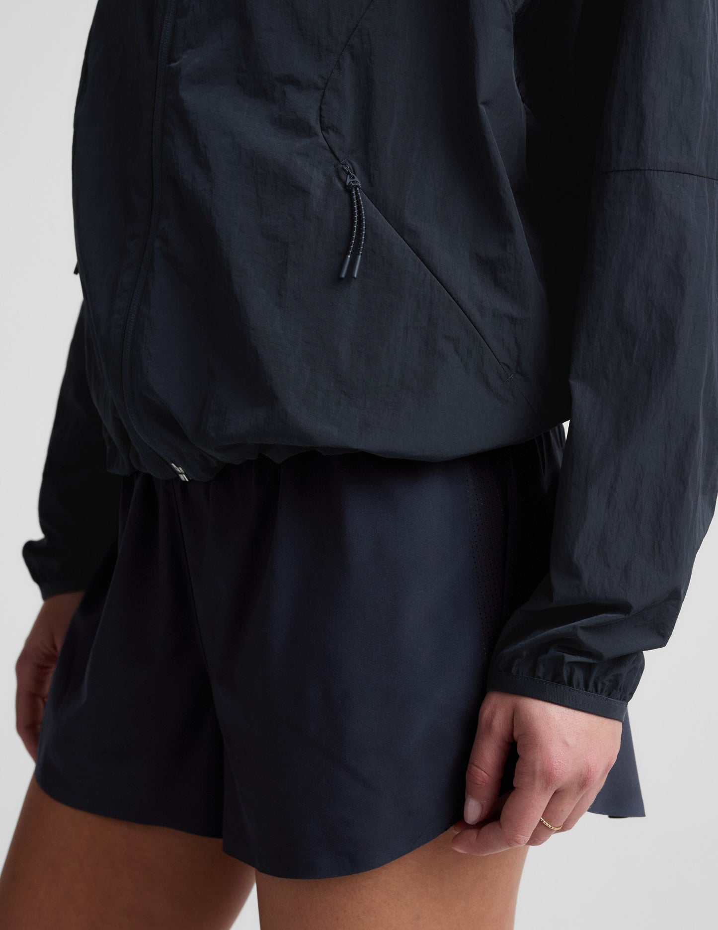 Woman wearing a blue hooded jacket and shorts against a plain background.