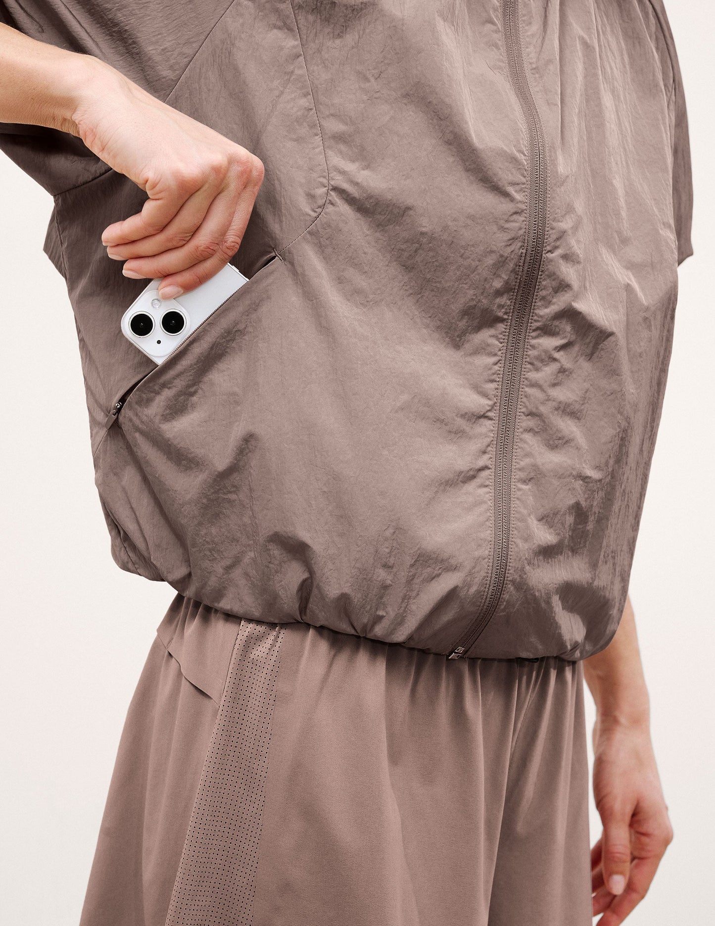 Woman wearing a brown hooded jacket and shorts on a light background.