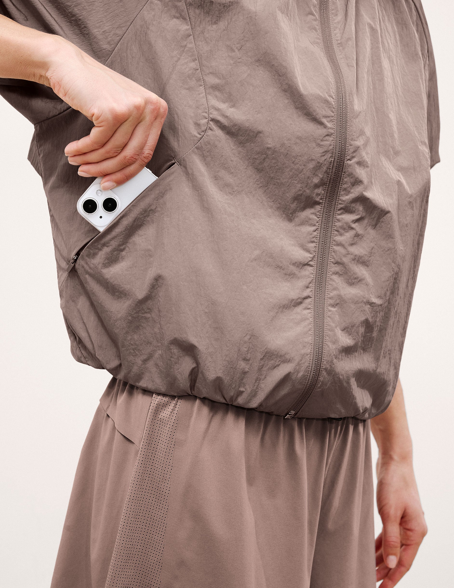 Woman wearing a brown hooded jacket and shorts on a light background.