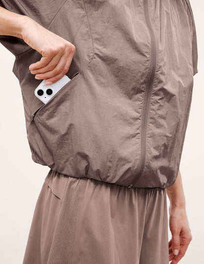 Woman wearing a brown hooded jacket and shorts on a light background.