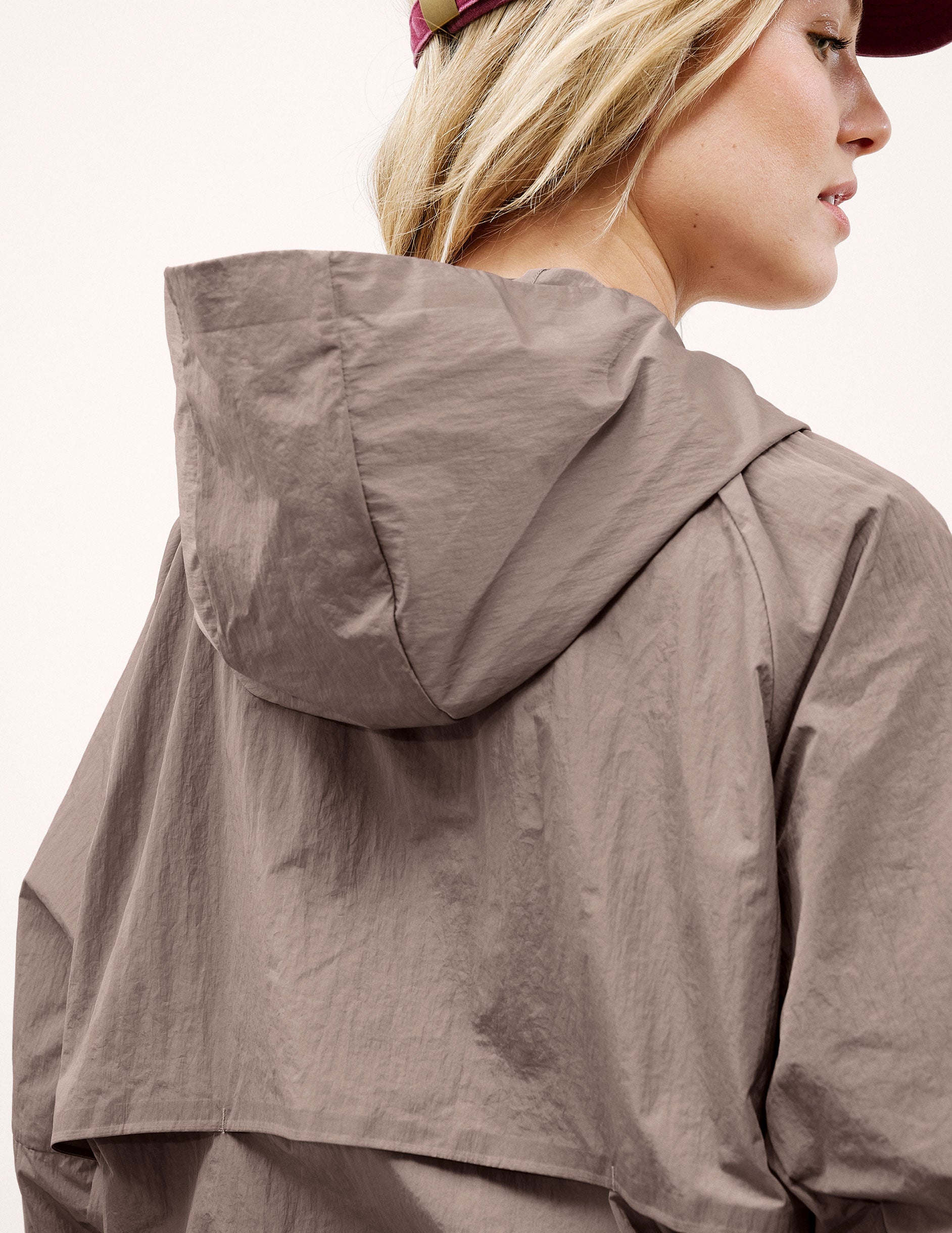 Woman wearing a brown hooded jacket and shorts on a light background.