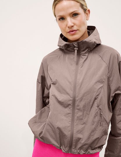 Woman wearing a brown hooded jacket on a light background.
