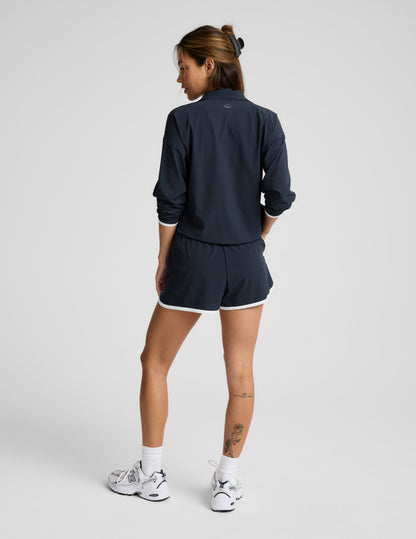 Woman wearing a blue quarter zip jacket and blue shorts with white trim against a plain background.