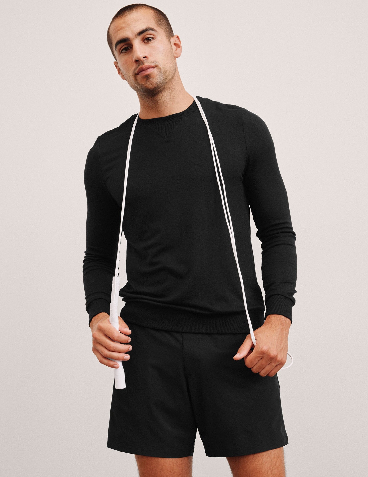 man wearing a black long-sleeve shirt and shorts on a light gray background.