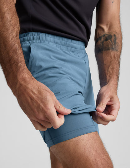 Close-up of blue Pivotal 2.0 Men's Lined Short 7" with a hand lifting the hem to reveal the built-in matching liner.