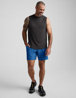 Man wearing Blue Pivotal 2.0 Men's Lined Short 7" with a grey sleeveless tank top and black sneakers.