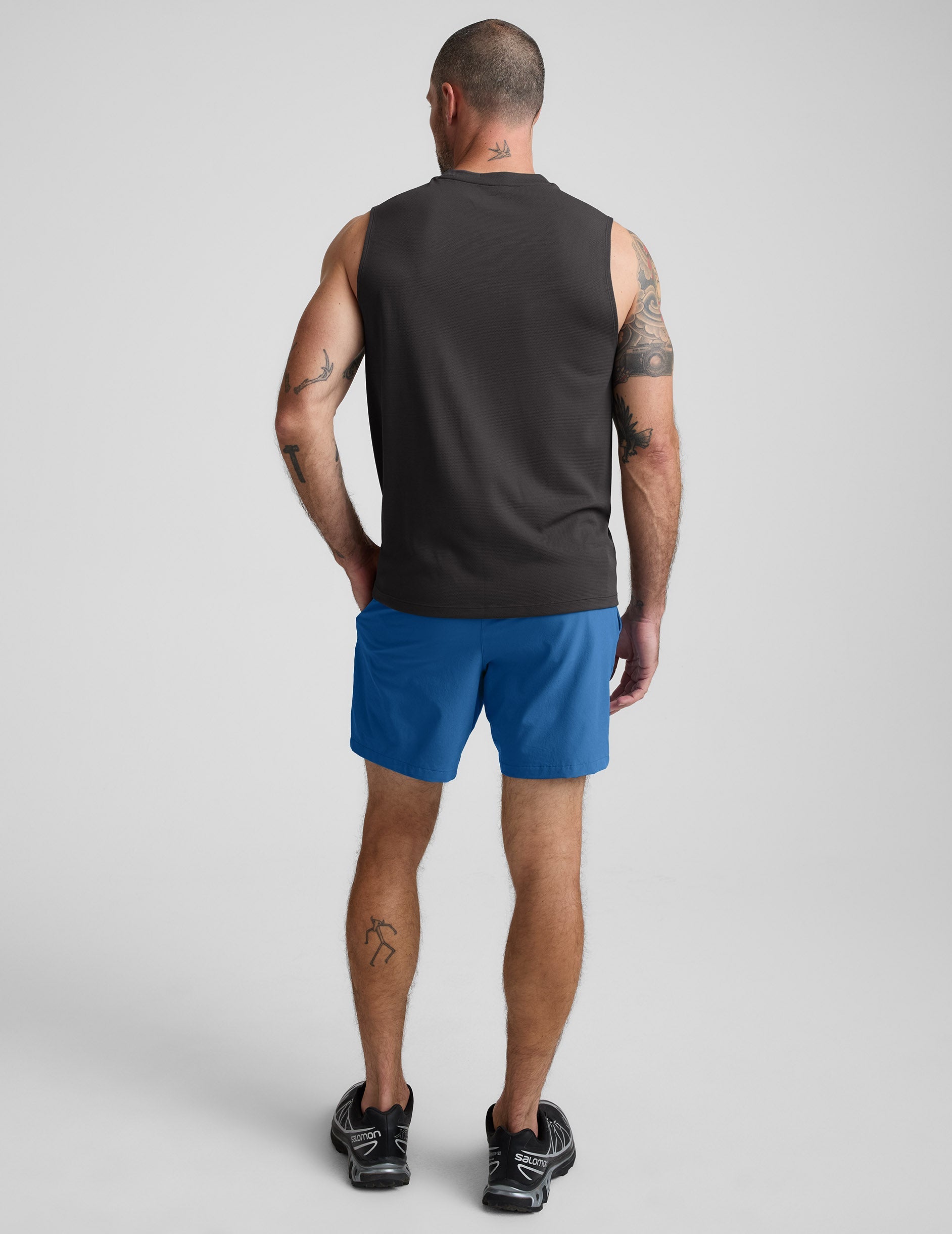 Man wearing Blue Pivotal 2.0™ Men's Lined Short 7" in a rear view, paired with a grey tank top and black sneakers.