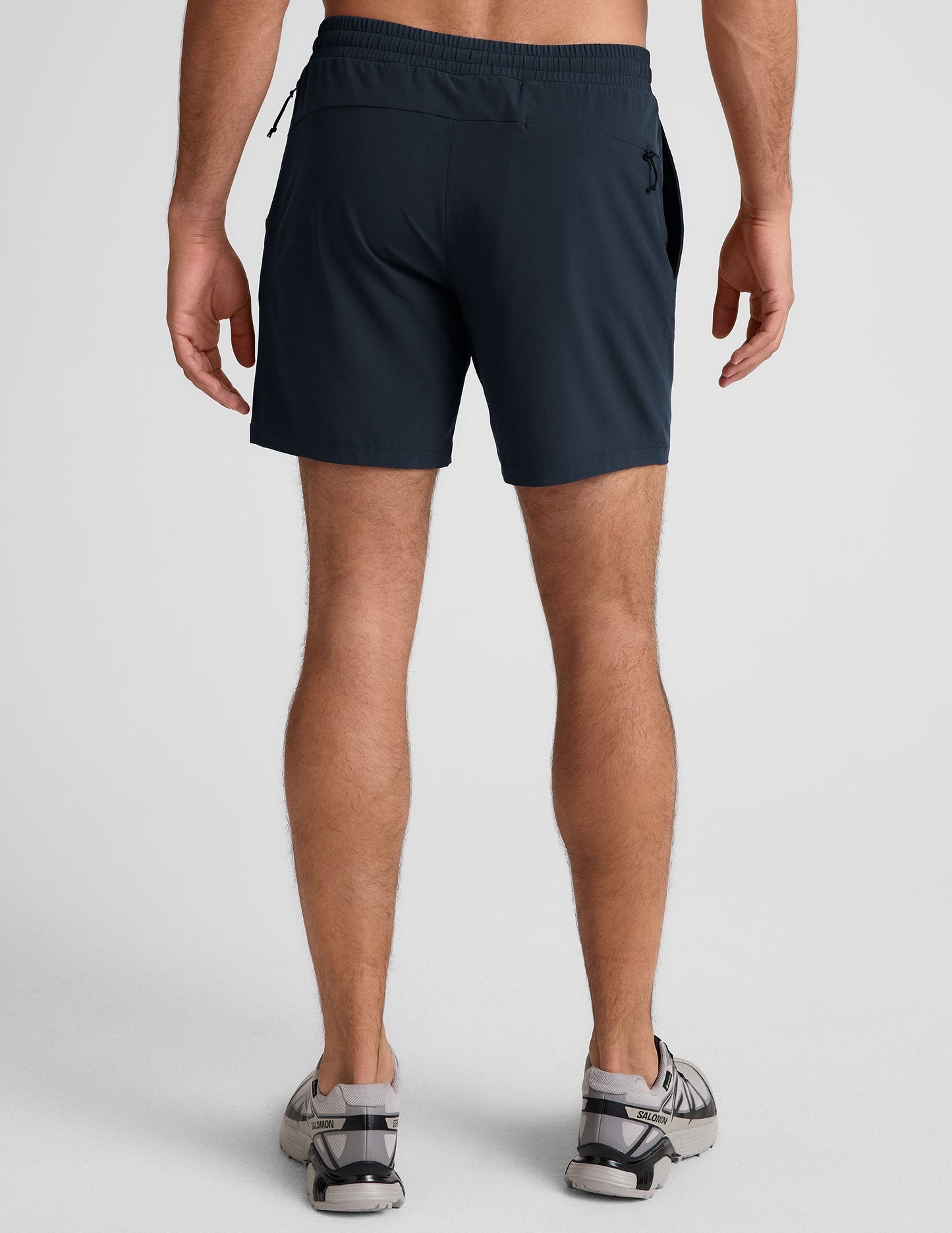 Rear view of navy Pivotal 2.0 Men's Lined Short 7" showing the elastic waistband and zipper pocket on a male model.