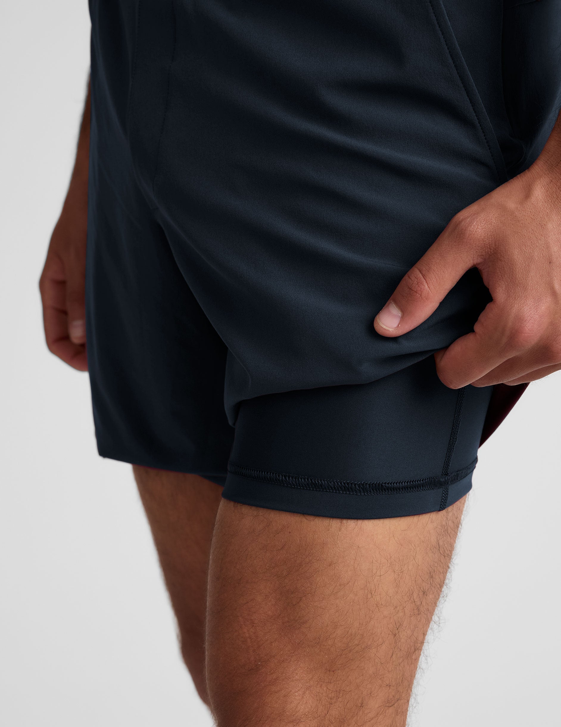Close-up of navy Pivotal 2.0 Men's Lined Short 7" with a hand lifting the hem to reveal the built-in interior lining.