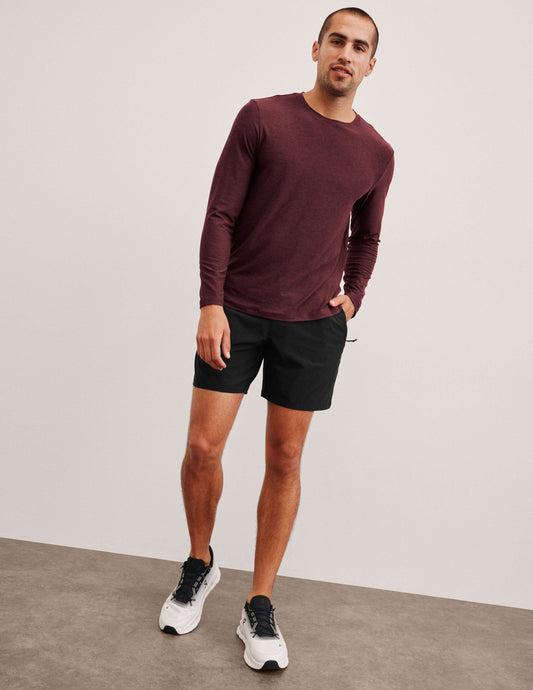 Man standing in black Pivotal 2.0 Men's Short 7 inch, relaxed fit, paired with a maroon long-sleeve shirt and sneakers.