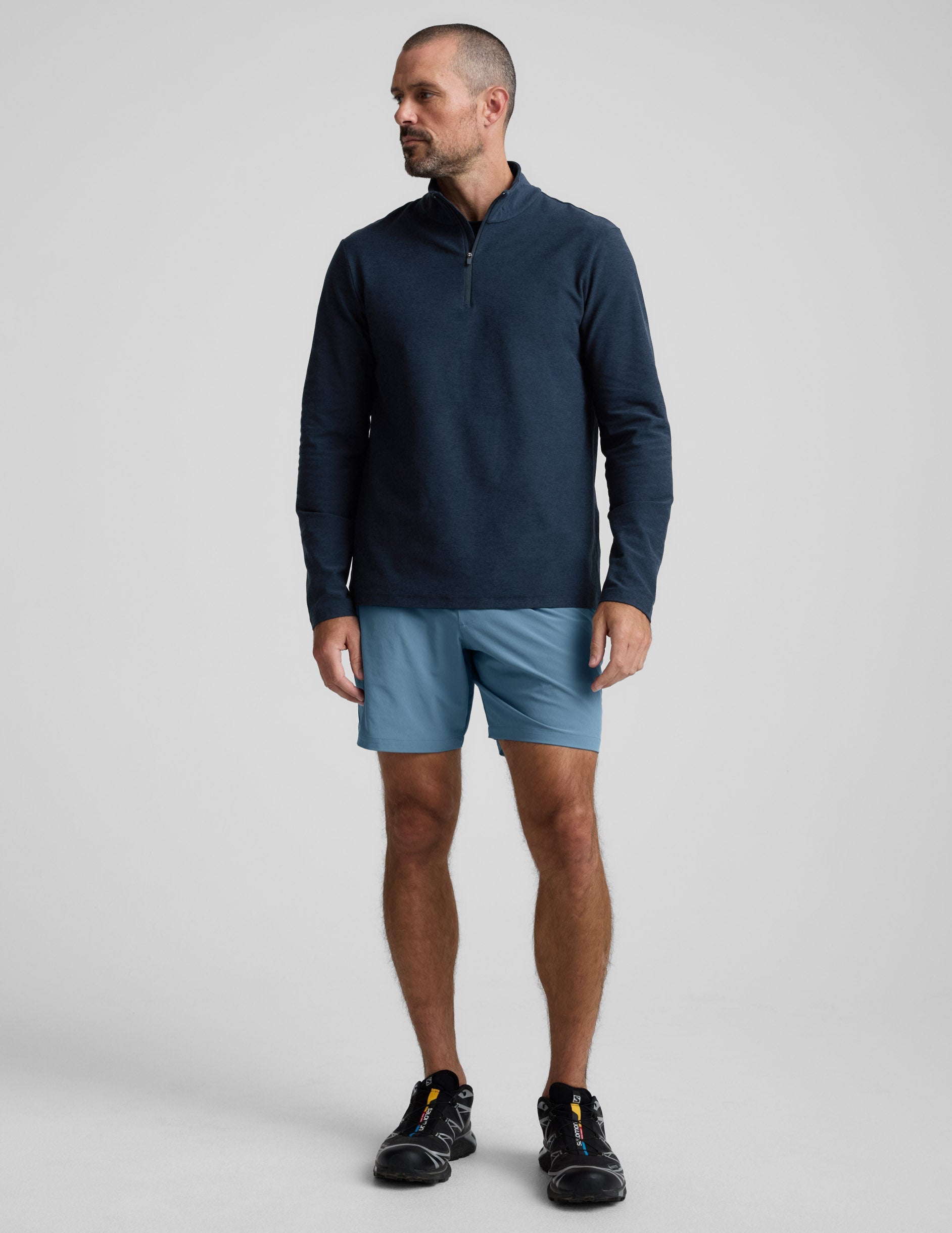 Man wearing Navy Pivotal 2.0™ Men's Short 7" paired with a navy quarter-zip pullover and black sneakers.