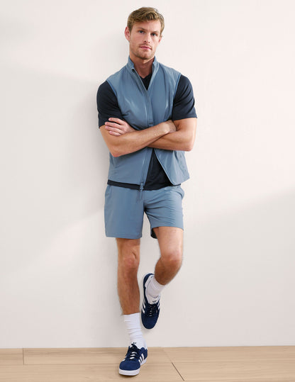 Man wearing Navy Pivotal 2.0 Men's Short 7"™ paired with a blue vest, black t-shirt, and white socks.