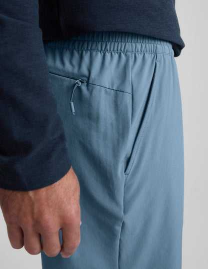 Man wearing Navy Pivotal 2.0 Men's Short 7"™ with a dark long-sleeve shirt, detailing the elastic waist and zipper pocket.