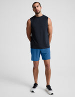 Man wearing Blue Pivotal 2.0 Men's Short 7"™ paired with a black sleeveless top and white sneakers.