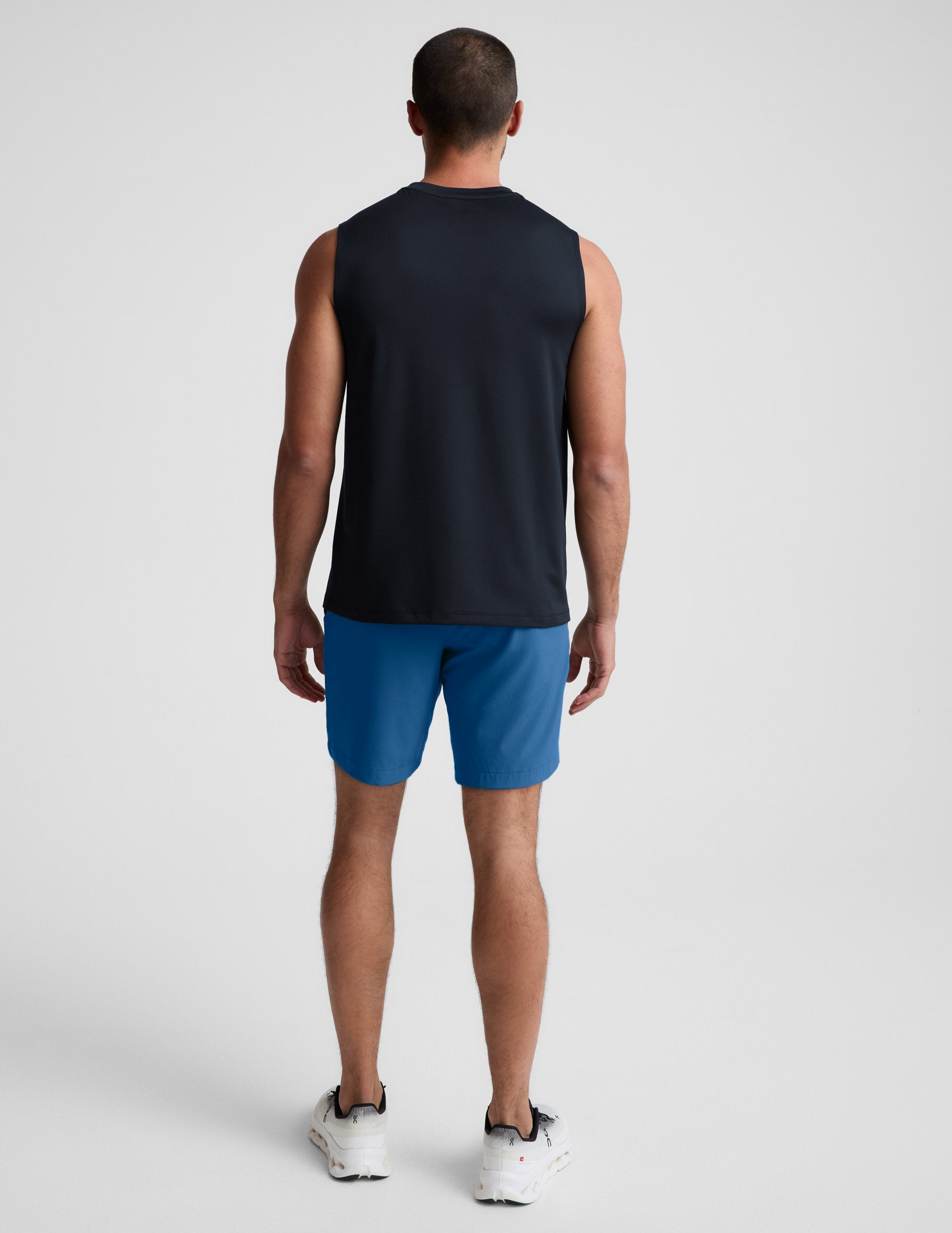 Man wearing Blue Pivotal 2.0 Men's Short 7™ from a rear view, paired with a black sleeveless top and white sneakers.