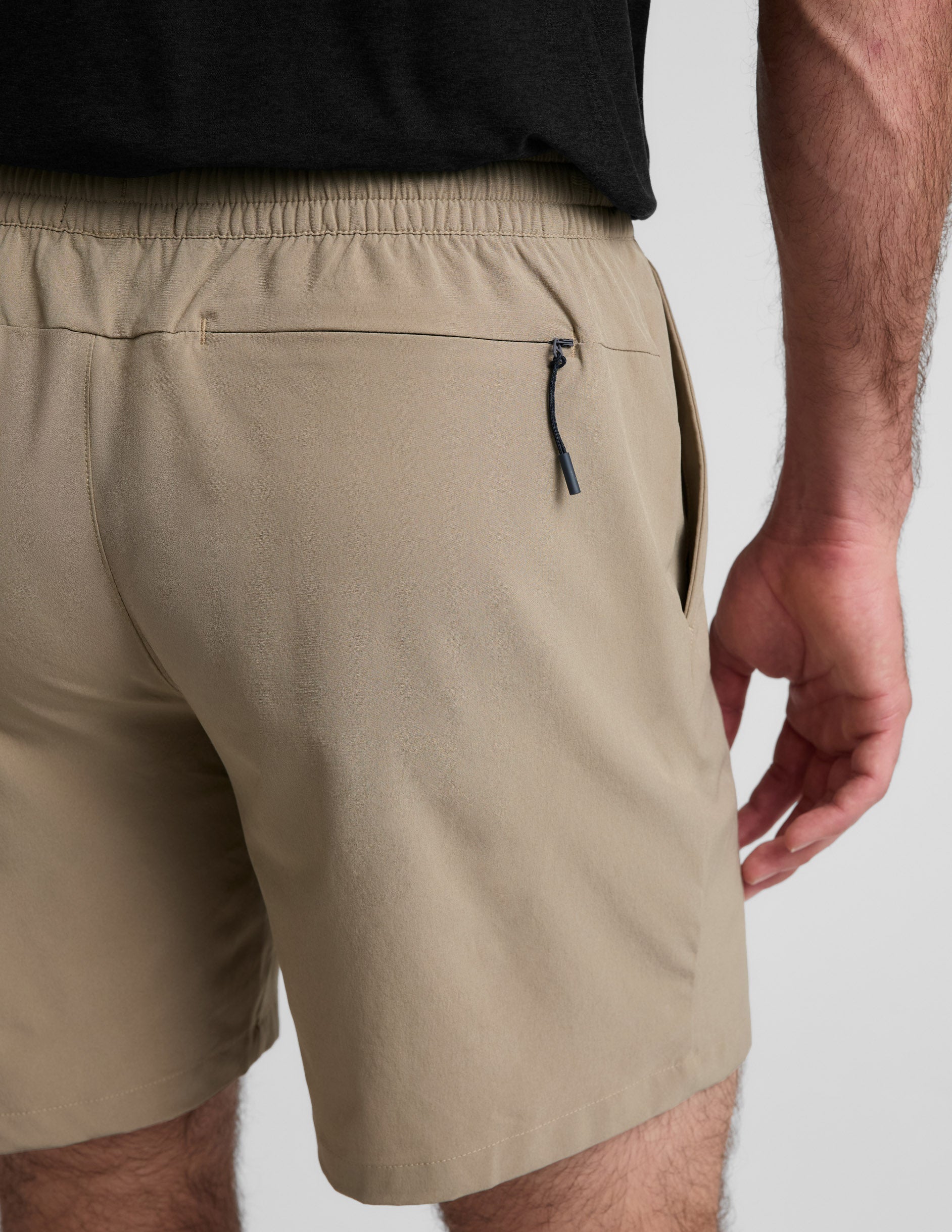 Back view of beige Pivotal 2.0 Men's Short 7" showing the elastic waistband, side pocket, and rear zippered pocket.