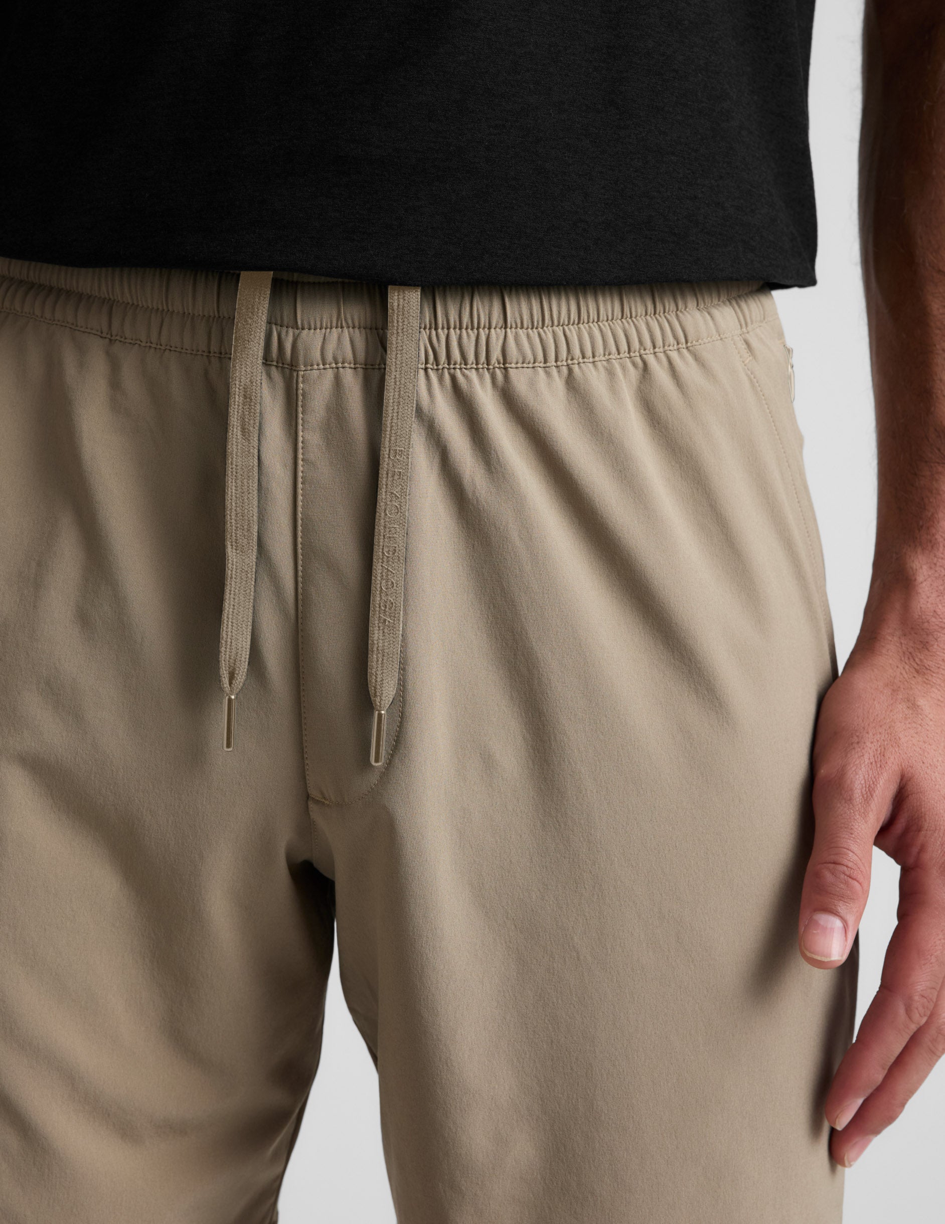 Close-up of the beige Pivotal 2.0 Men's Short 7" showing the elastic waistband and flat drawcord on a person.