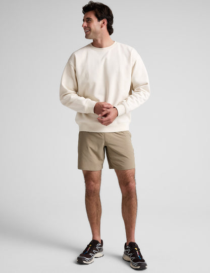 Man wearing beige Pivotal 2.0 Men's Short 7 inch running shorts and a cream sweatshirt in a standing studio portrait.