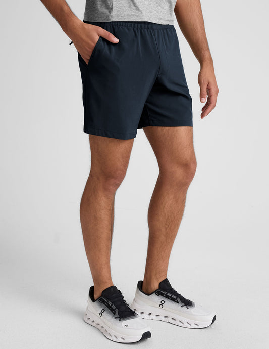 Relaxed navy Pivotal 2.0 Men's Short 7" with side pockets and elastic waist on a model wearing white sneakers.