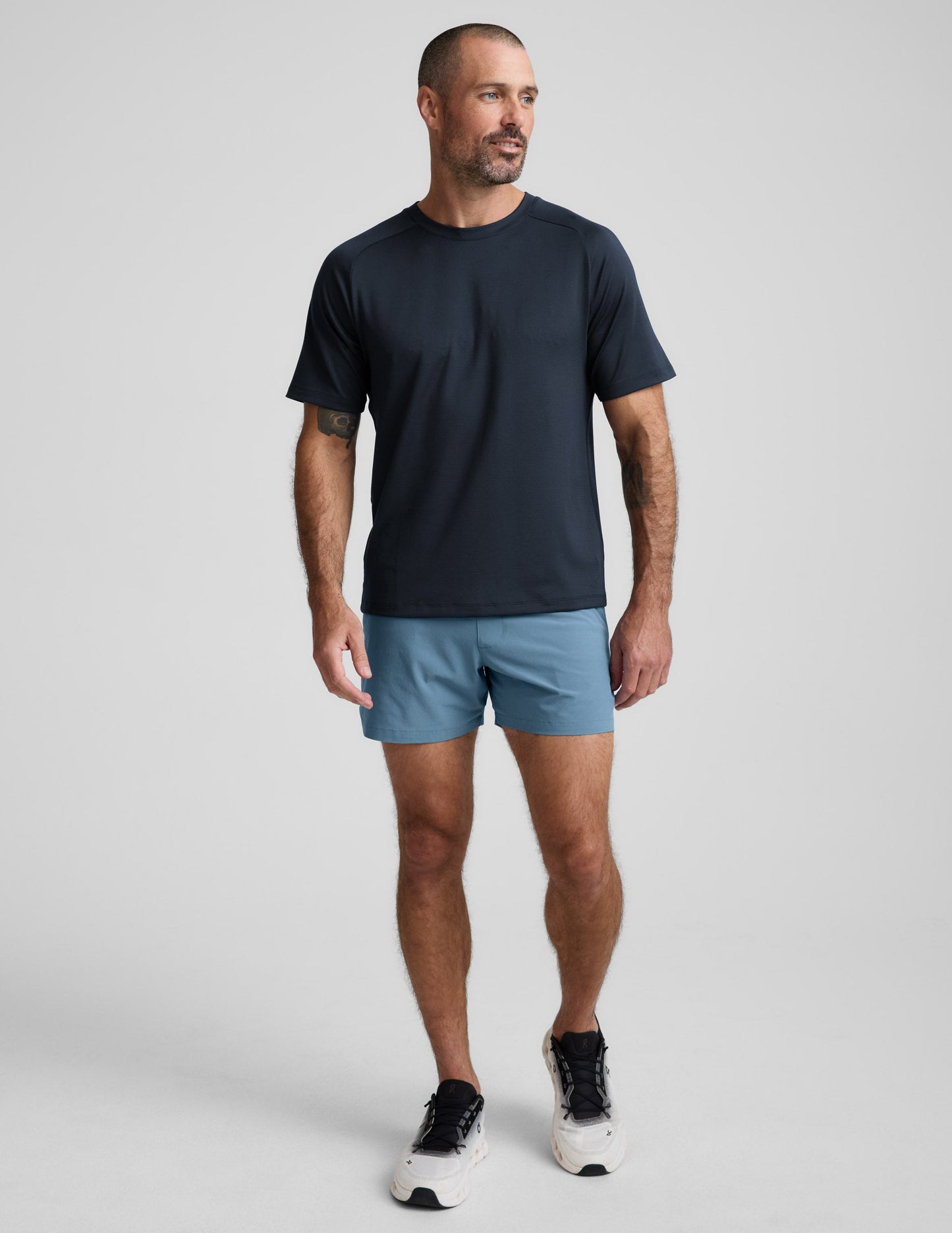Front view of a man in blue Pivotal 2.0 Men's Lined Short 5" with a relaxed fit and mid-thigh length on a grey background.