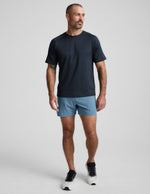 Front view of a man in blue Pivotal 2.0 Men's Lined Short 5" with a relaxed fit and mid-thigh length on a grey background.