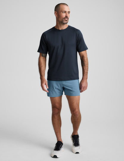 Front view of a man in blue Pivotal 2.0 Men's Lined Short 5" with a relaxed fit and mid-thigh length on a grey background.