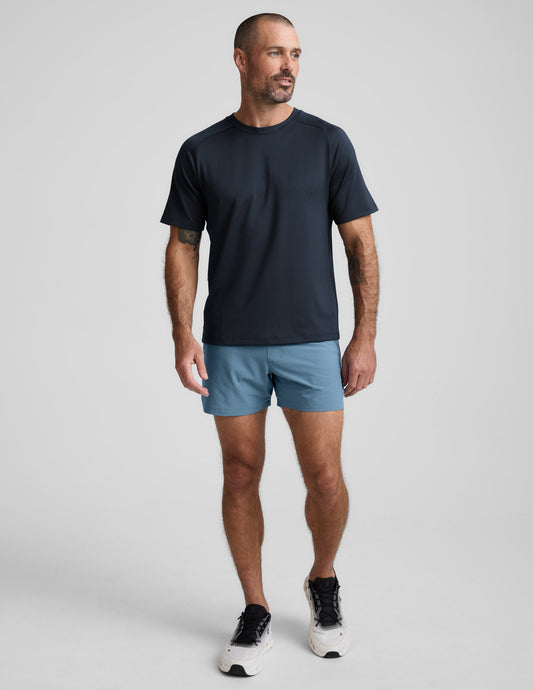 Front view of a man in blue Pivotal 2.0 Men's Lined Short 5" with a relaxed fit and mid-thigh length on a grey background.