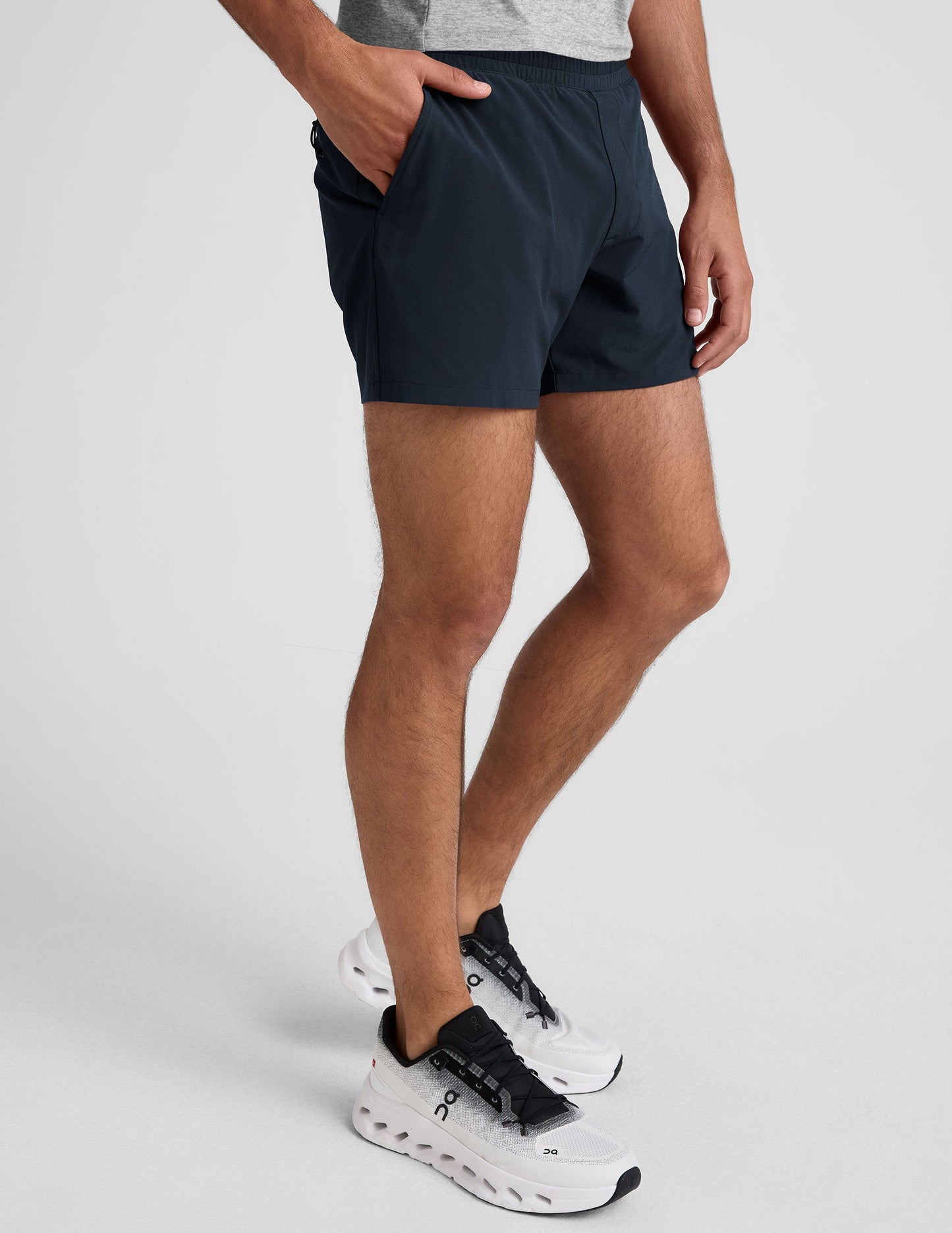 Side view of navy Pivotal 2.0 Men���s Lined Short 5" with an elastic waistband and side pocket, worn with white sneakers.