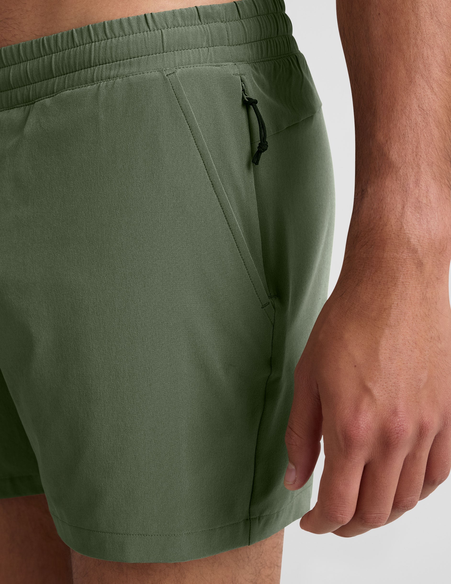 Side view of olive Pivotal 2.0 Men's Lined Short 5" on a person, showing the elastic waistband and side zipper pocket.