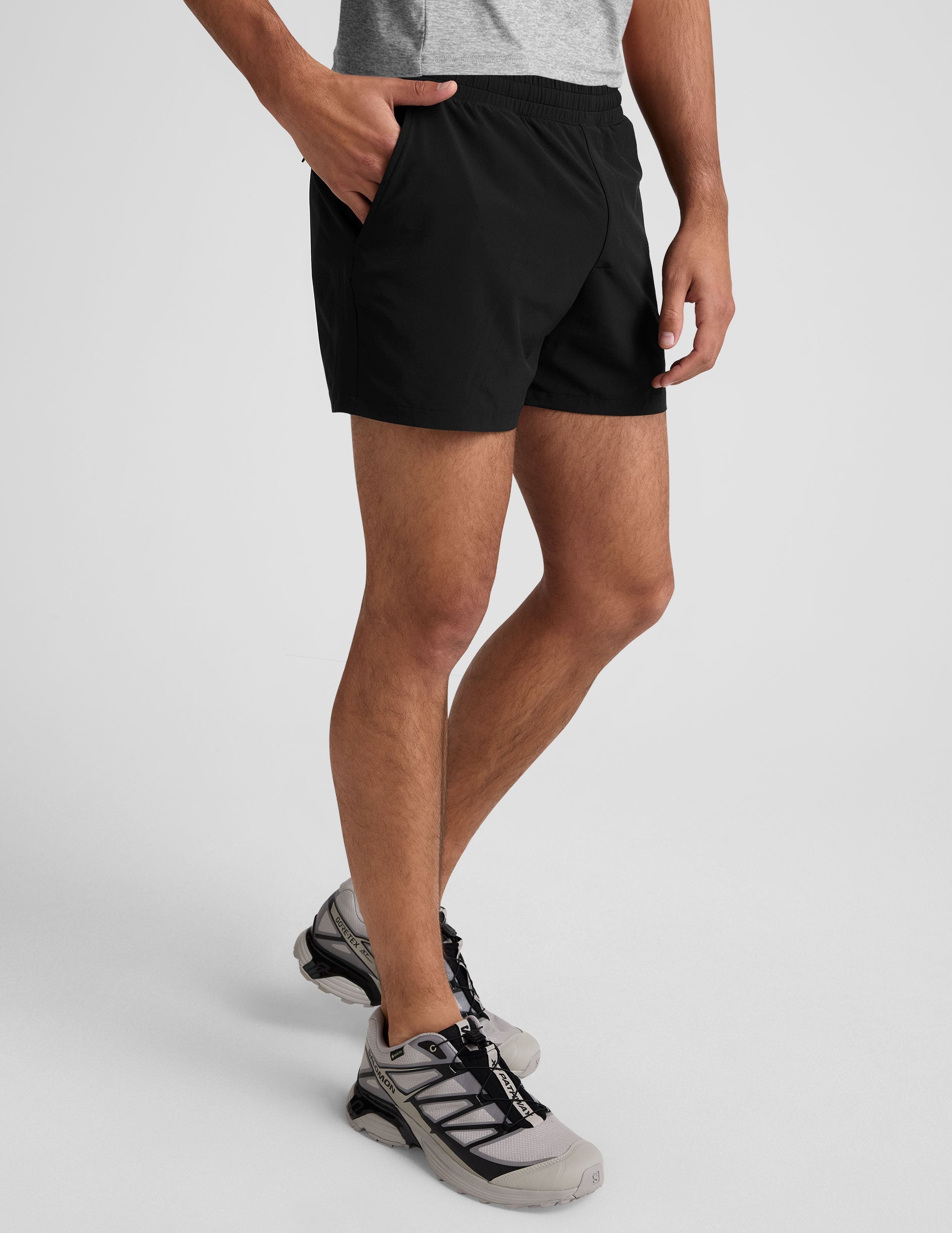 A man wears black Pivotal 2.0 Men's Lined 5" Shorts with an elastic waistband, side pockets, and a mid-thigh length.