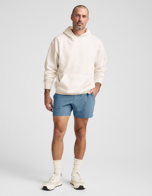 A man wearing blue Pivotal 2.0 Men's Short 5" with a cream hoodie. Relaxed-fit 5-inch inseam athletic shorts with pockets.