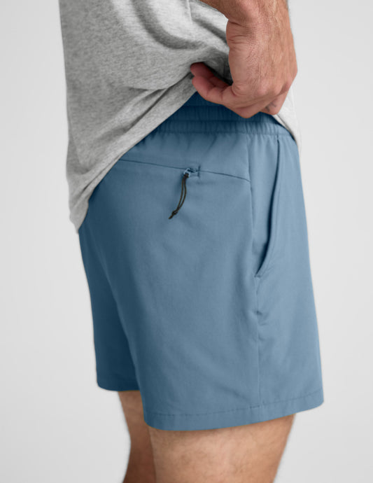 Side view of blue Pivotal 2.0 Men's Short 5" showing the elastic waistband and a zippered back pocket on a model's hip.