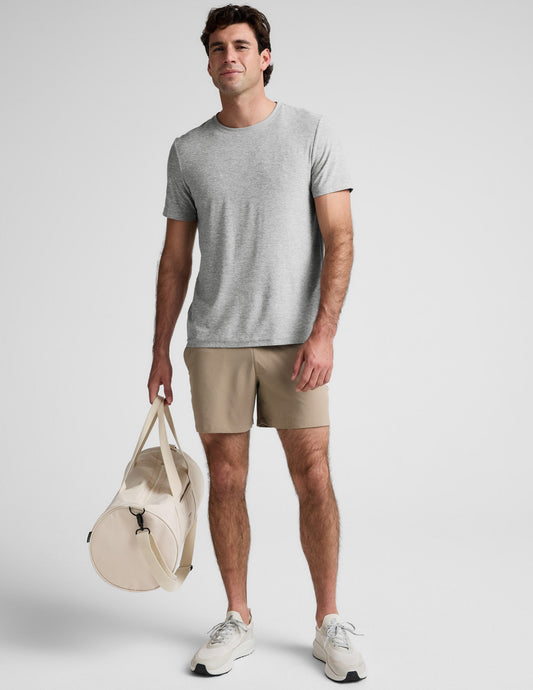 Front view of a man wearing beige Pivotal 2.0 Men's Short 5" with a grey t-shirt and gym bag against a neutral background.