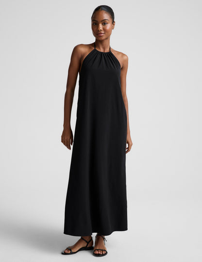 Woman wearing a black halter neck dress on a plain background.