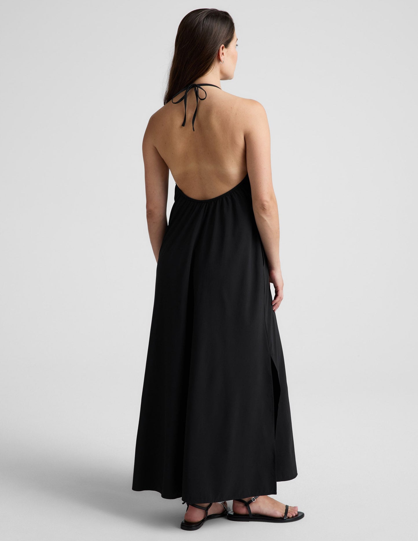 Woman wearing a black halter neck dress on a light gray background.