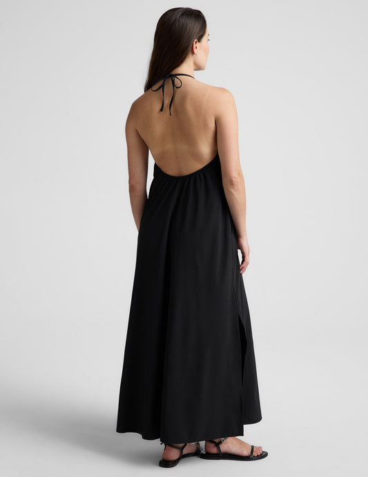 Woman wearing a black halter neck dress on a light gray background.
