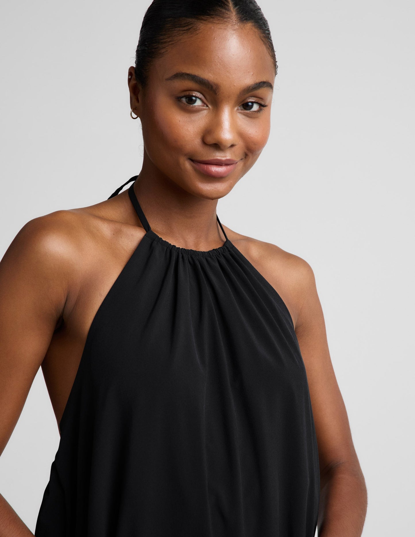 Woman wearing a black halter neck dress on a plain background.