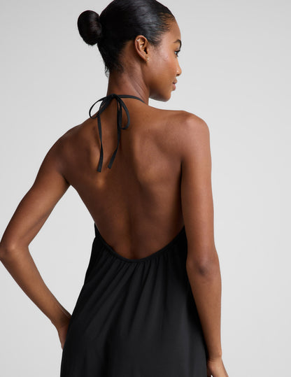Woman wearing a black halter neck dress on a plain background.