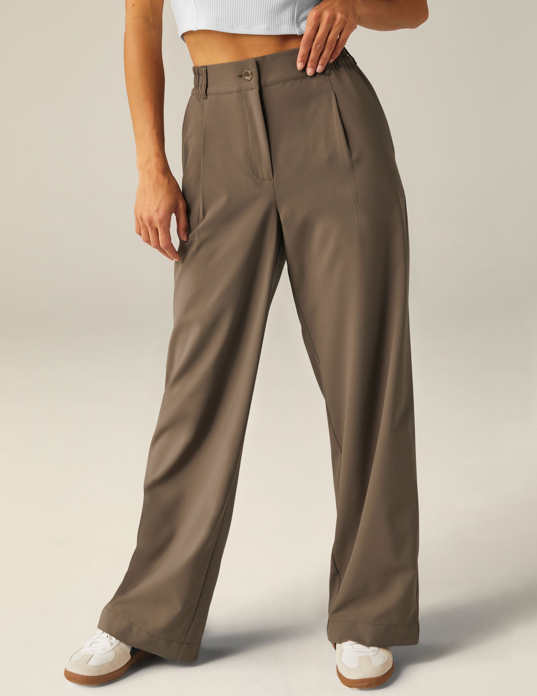 Status Wide Leg Trousers in brown with front pleats, zip fly, and a relaxed straight leg, paired with white sneakers.