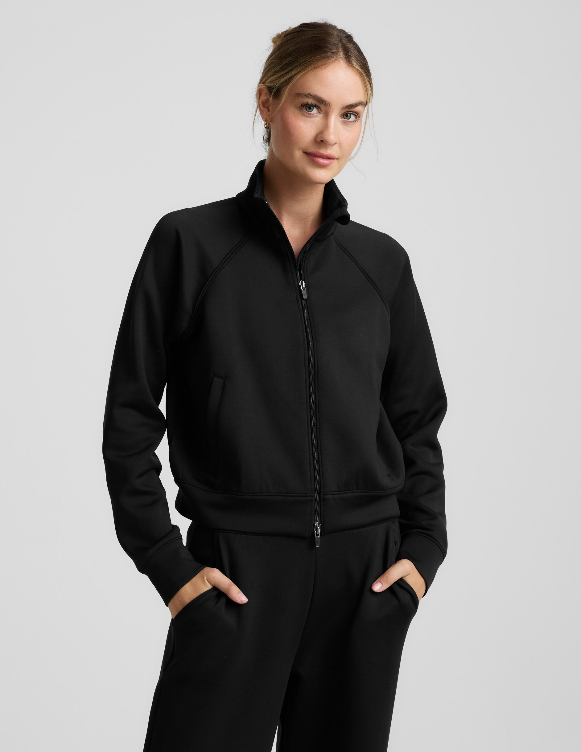 Woman wearing a black tracksuit on a light gray background.