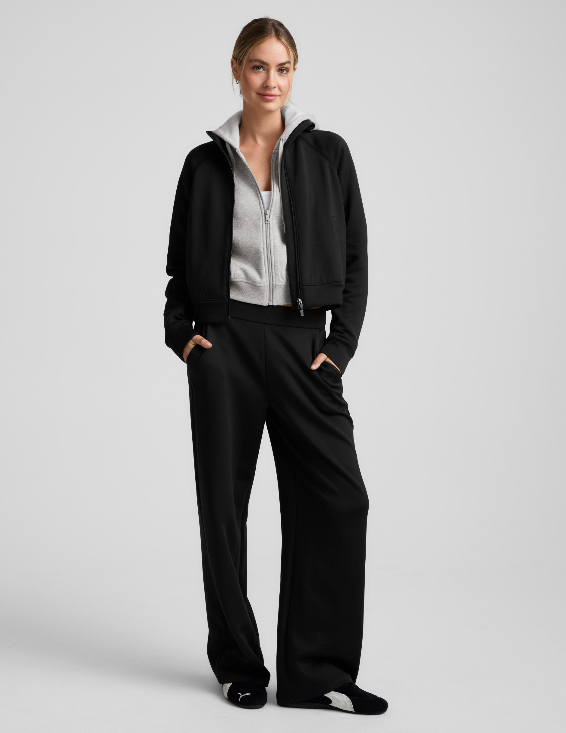 Woman wearing a black tracksuit on a light gray background.