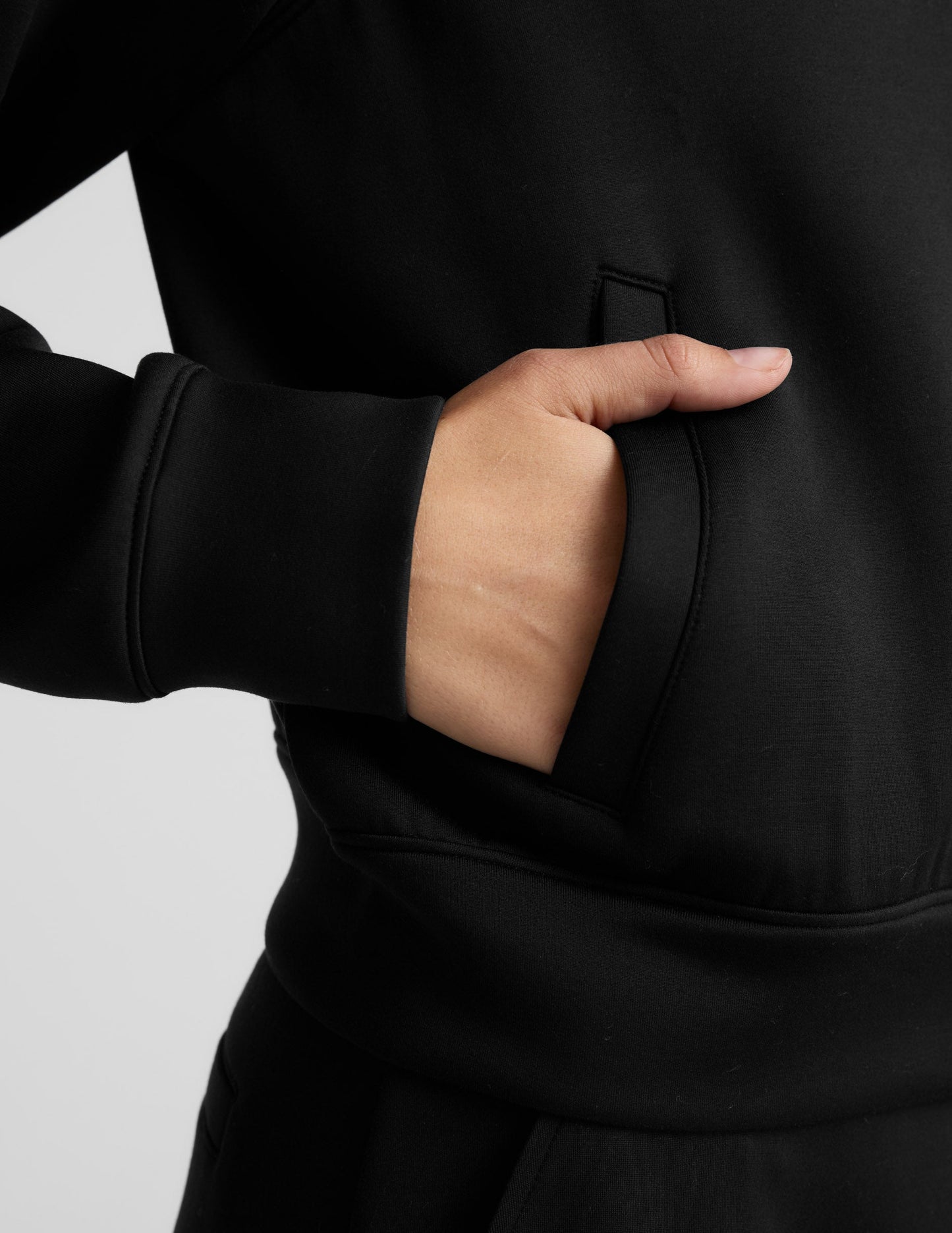 Woman wearing a black tracksuit on a light gray background.