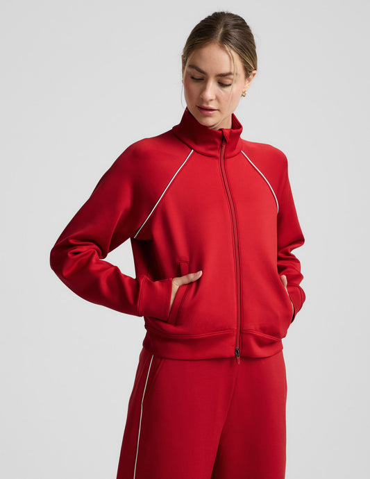 Woman wearing a red jacket with white piping against a plain background.