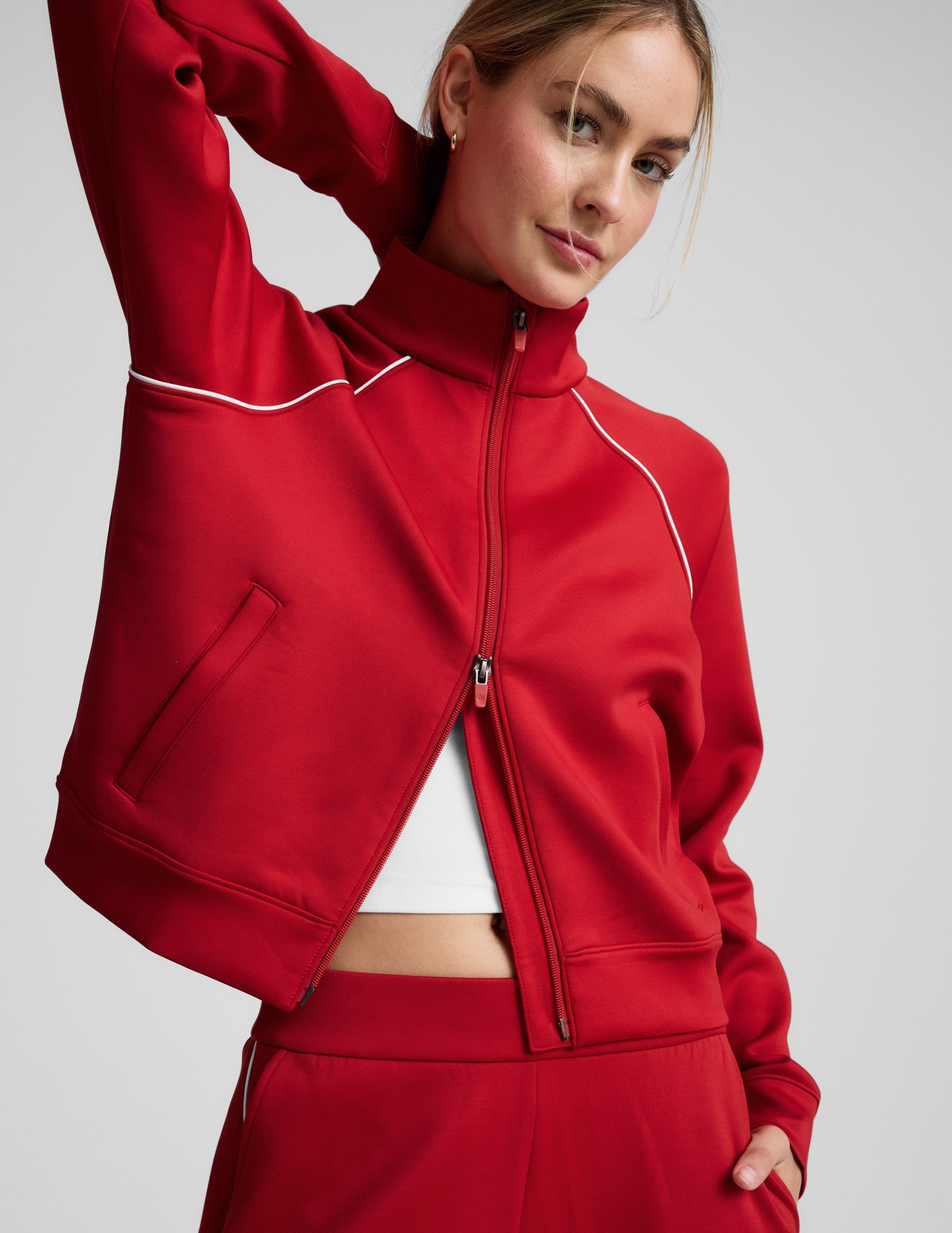 Woman wearing a red jacket with white piping against a plain background.