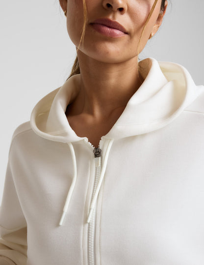 Woman wearing a white zip-up hoodie and black shorts against a plain background.