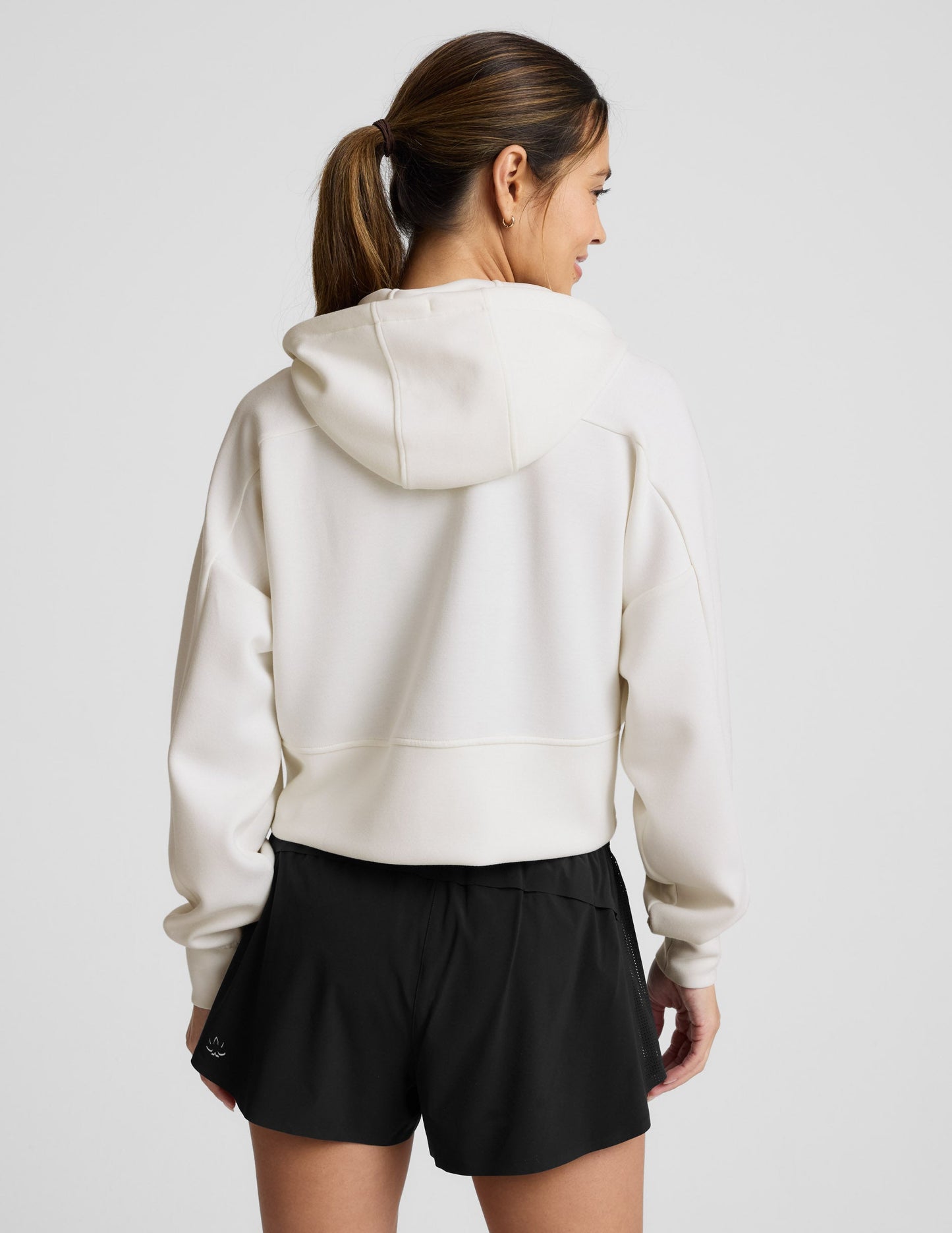 Woman wearing a white zip-up hoodie and black shorts against a plain background.