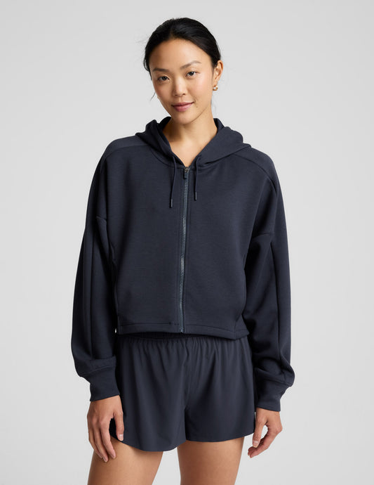 Woman is wearing a blue zip-up jacket and shorts against a plain background.
